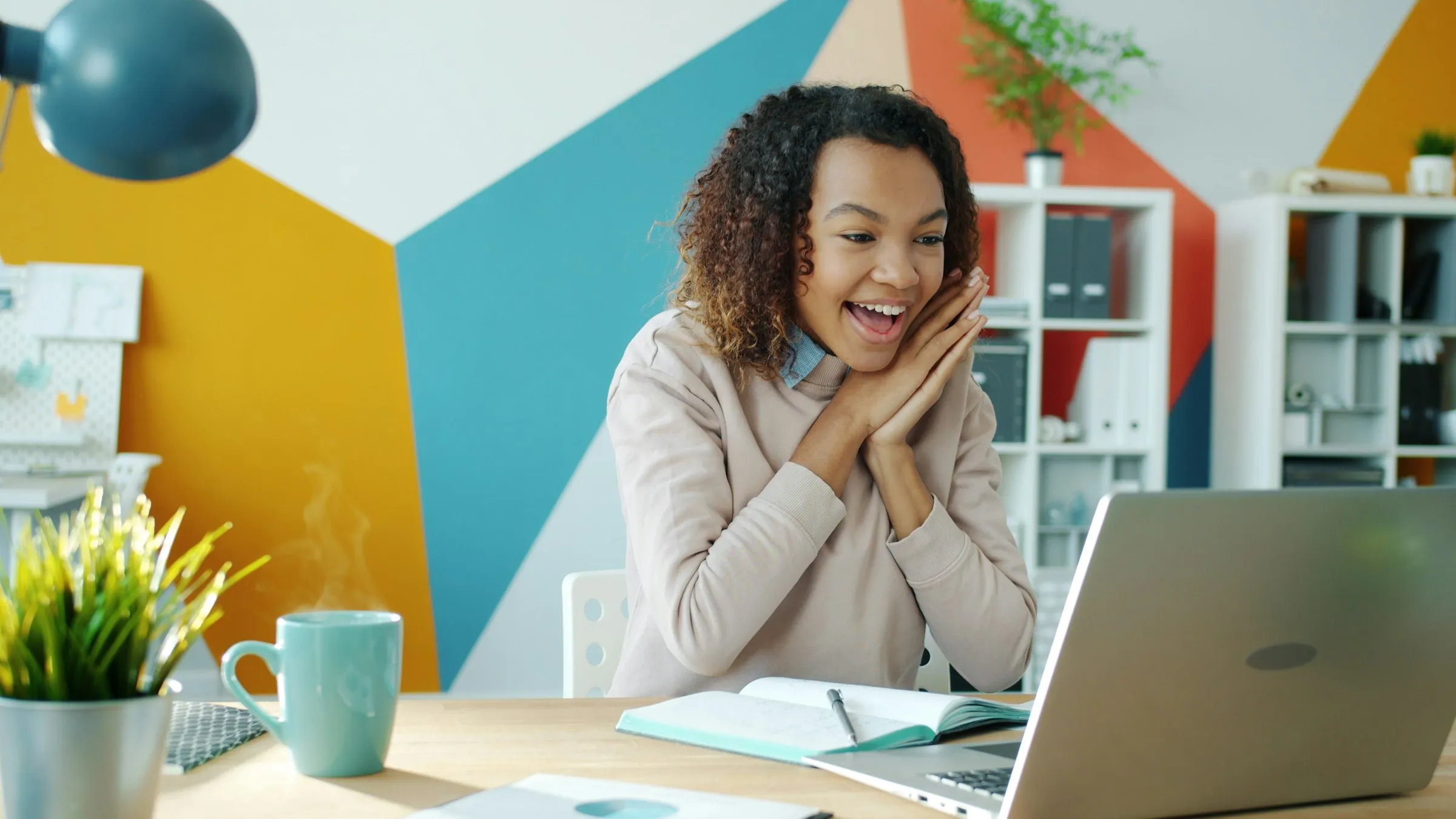 Excited woman smiling at her laptop beside a cup of coffee